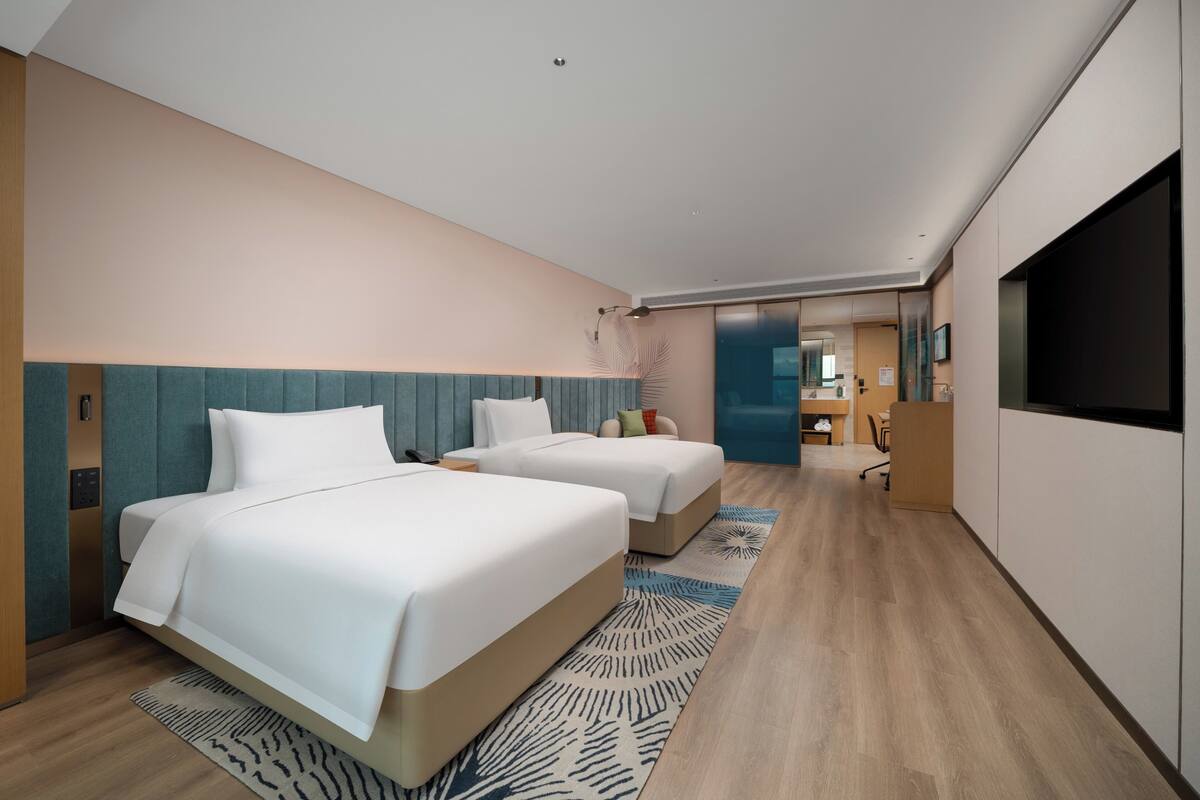 A modern hotel room with two beds, a desk, and a TV.