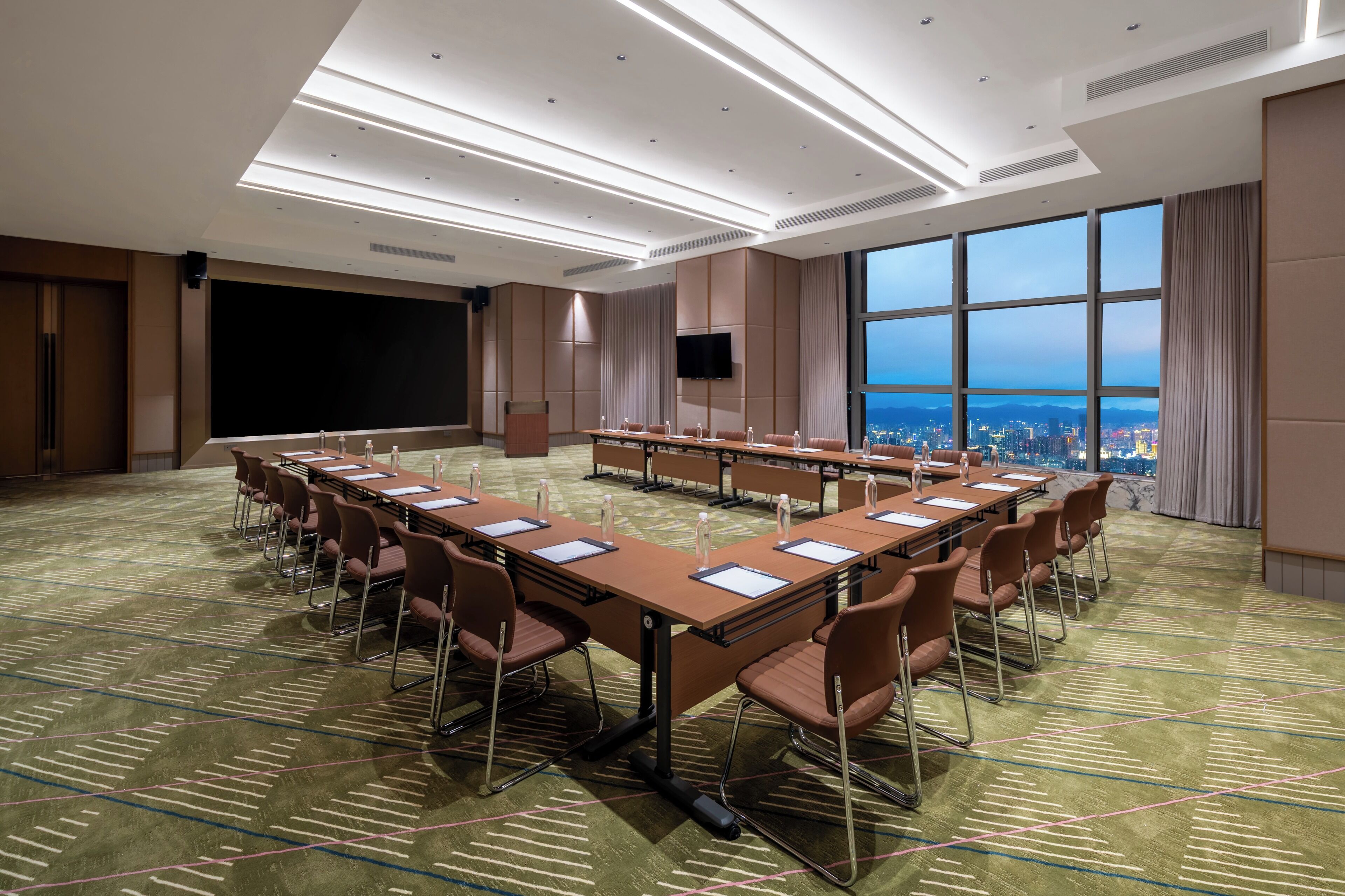 Une salle de conférence avec une longue table, des chaises, un écran et une vue sur la ville.