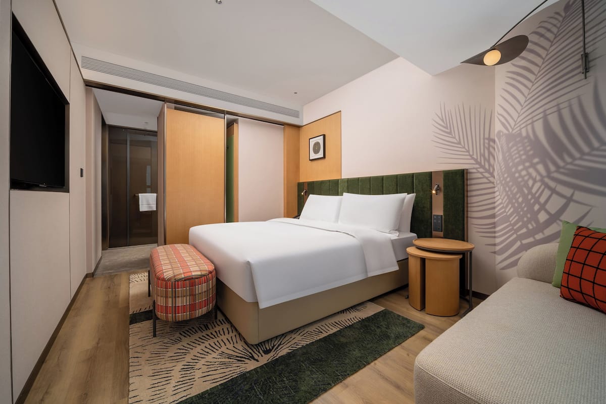 A modern hotel room with a large bed, a small seating area, and a television.