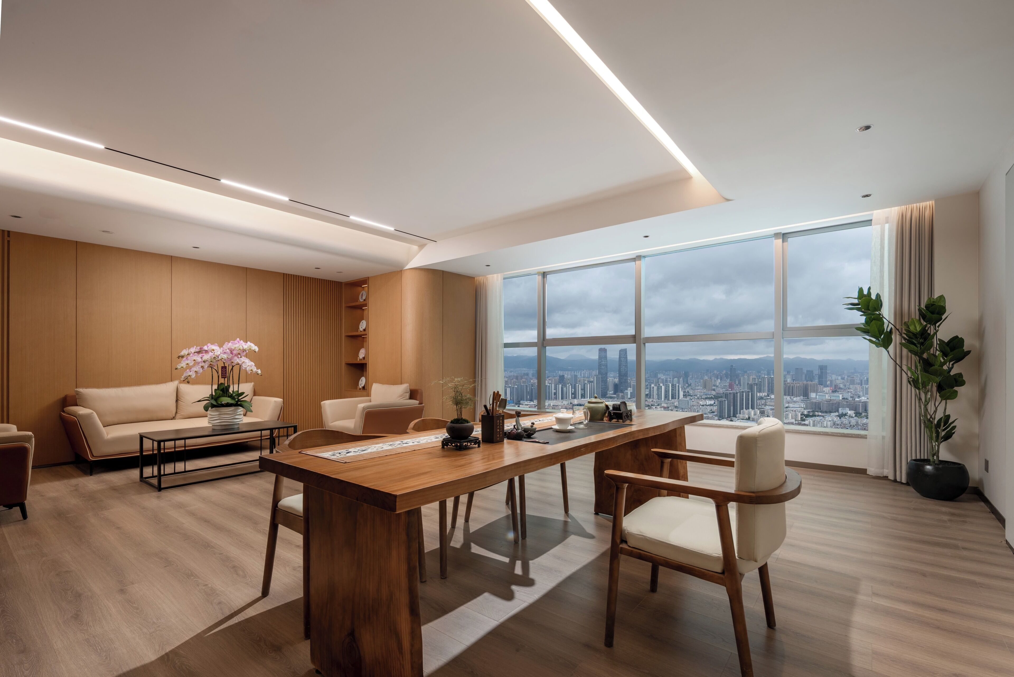 A modern office with a large wooden desk, leather sofas, and a city view through large windows.