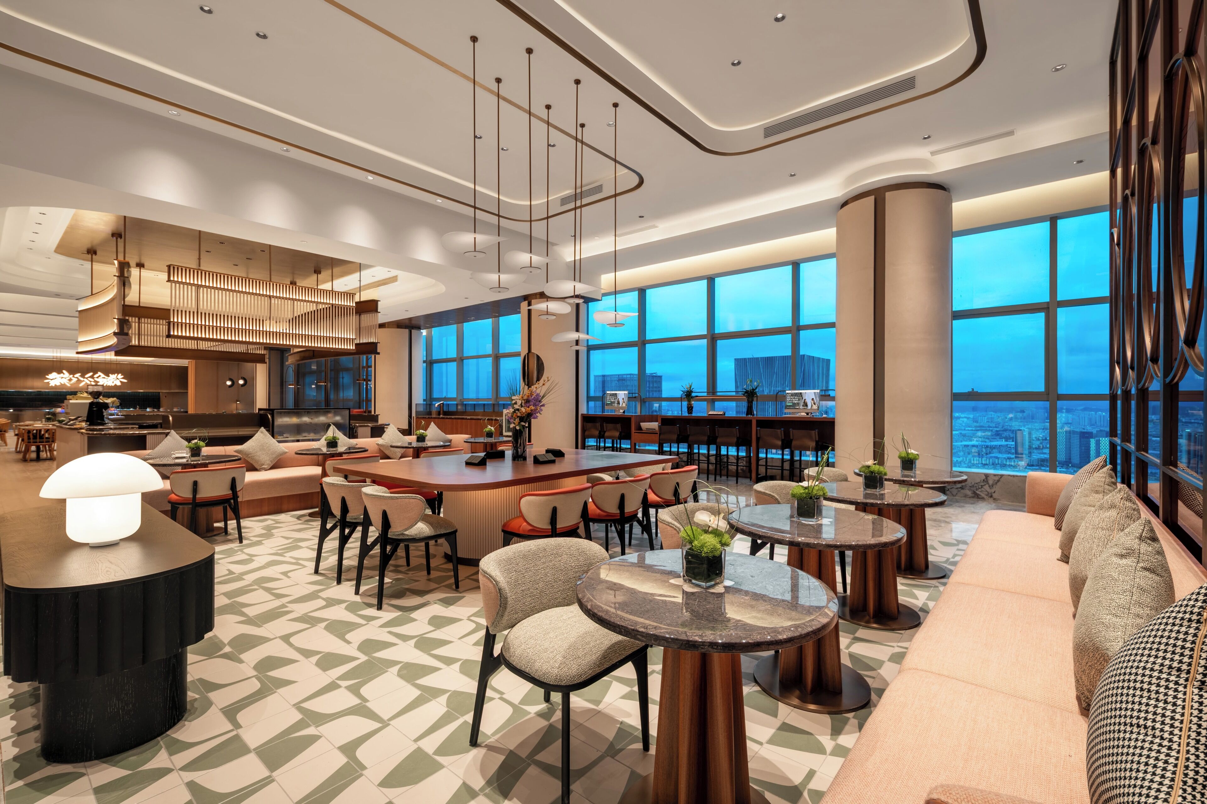 A modern hotel lobby with a bar, seating areas, and large windows offering city views.