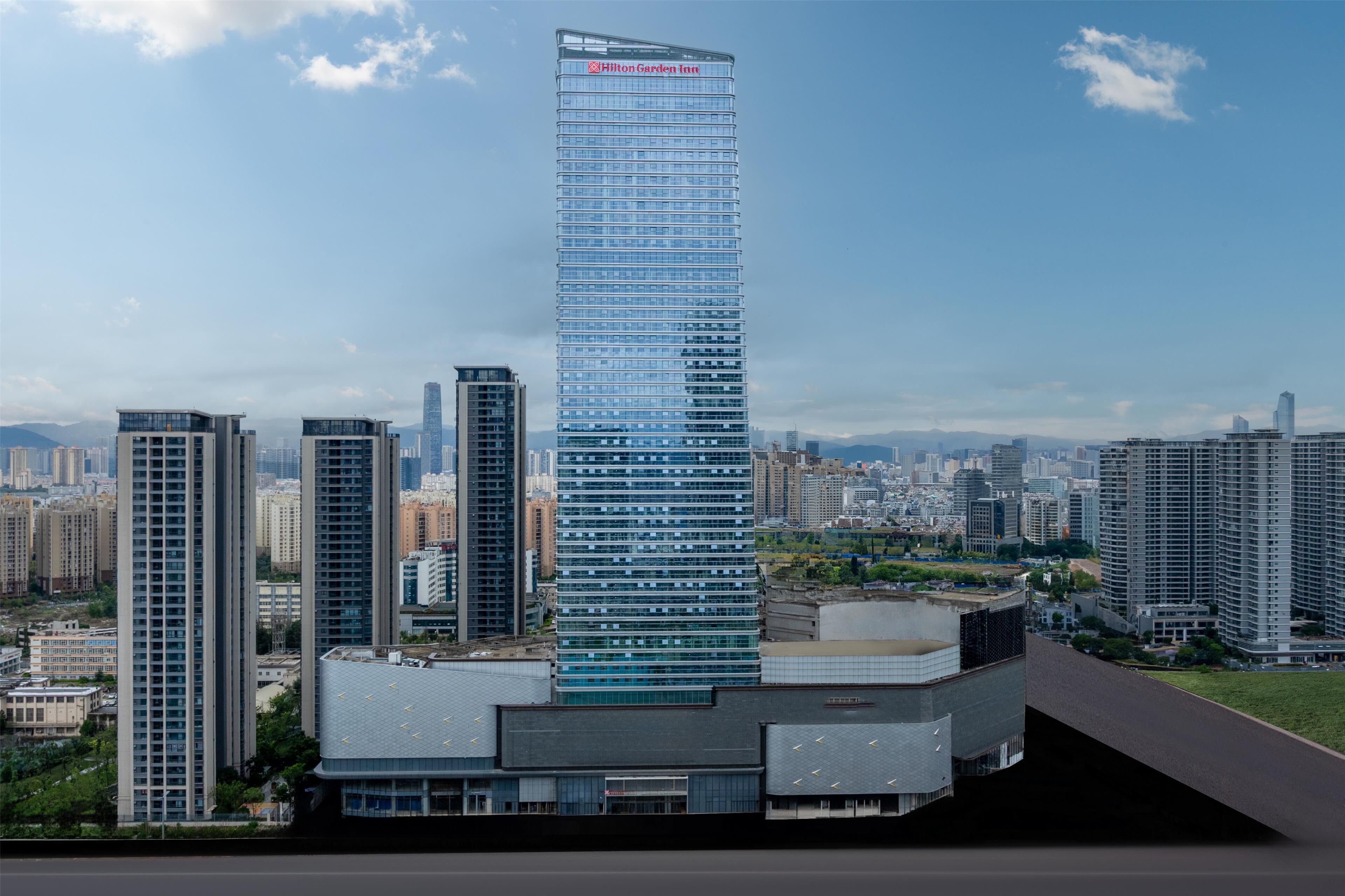 Un hôtel moderne, situé dans un immeuble de grande hauteur et doté d’une façade en verre, entouré d’autres bâtiments imposants au cœur d’un paysage urbain.