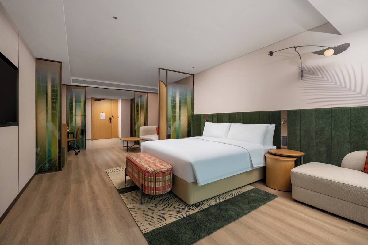 A modern hotel room with a large bed, a sofa, a small table, and a TV.
