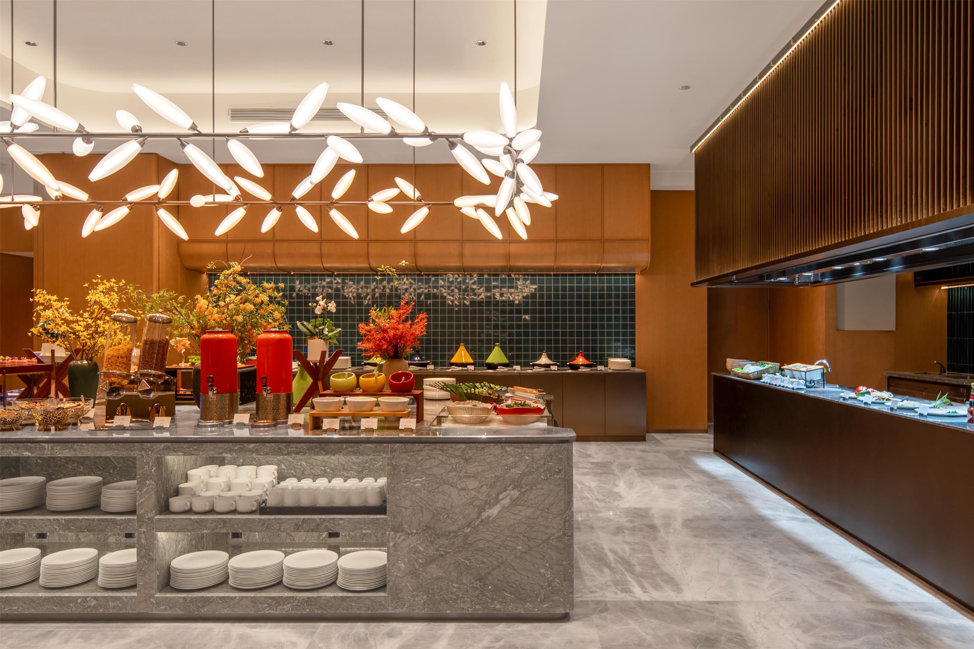 A modern hotel lobby with a marble reception desk, a variety of colorful flowers, and a unique ceiling light fixture.