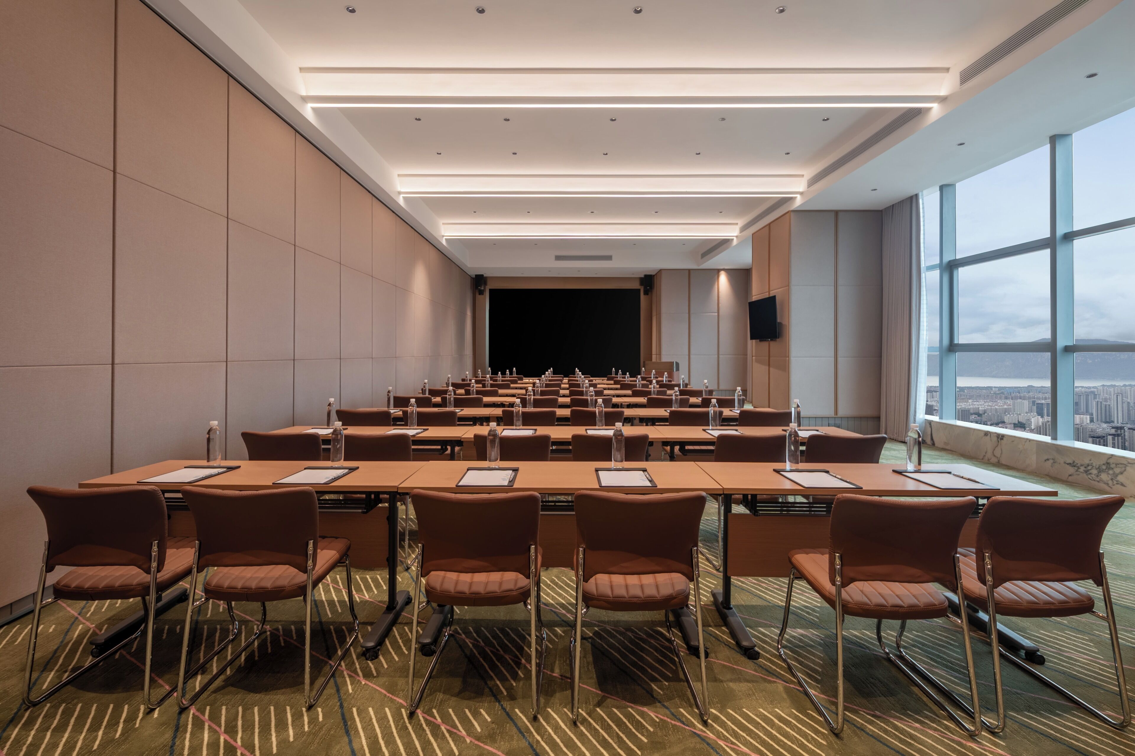 A conference room with a long table, multiple chairs, and a large window offering a city view.