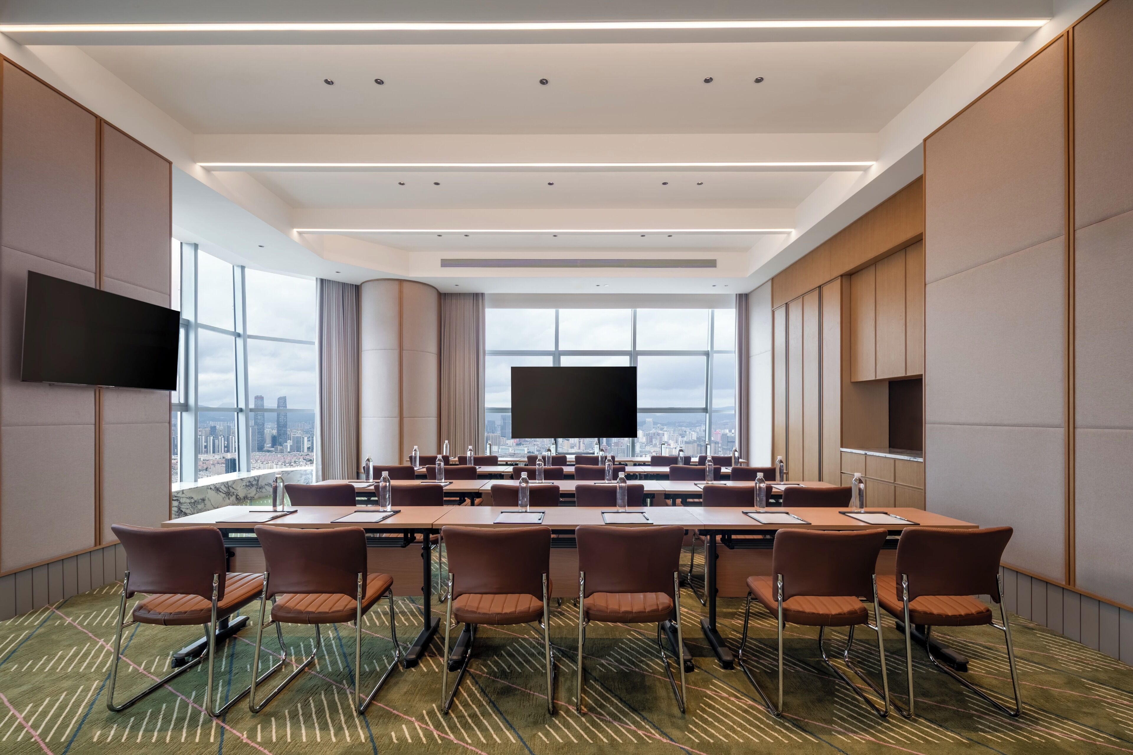 A conference room with a large table, multiple chairs, a flat-screen TV, and large windows offering a city view.