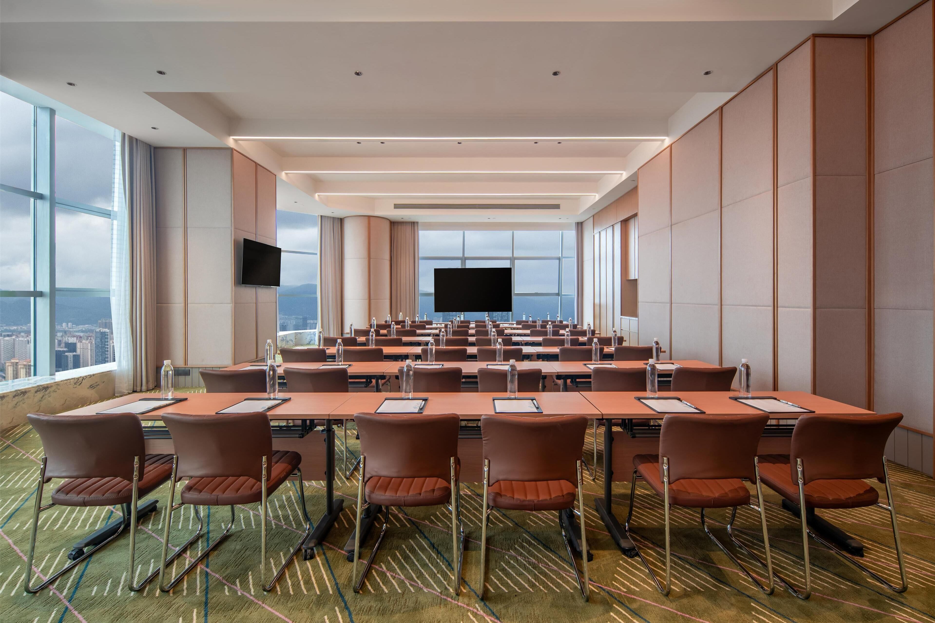 A conference room with a large table, chairs, a flat-screen TV, and a city view through large windows.