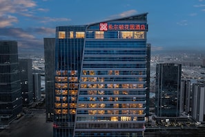 A modern high-rise building with a prominent logo at the top. - Hilton Garden Inn Kunming Railway Station South (Kunming)