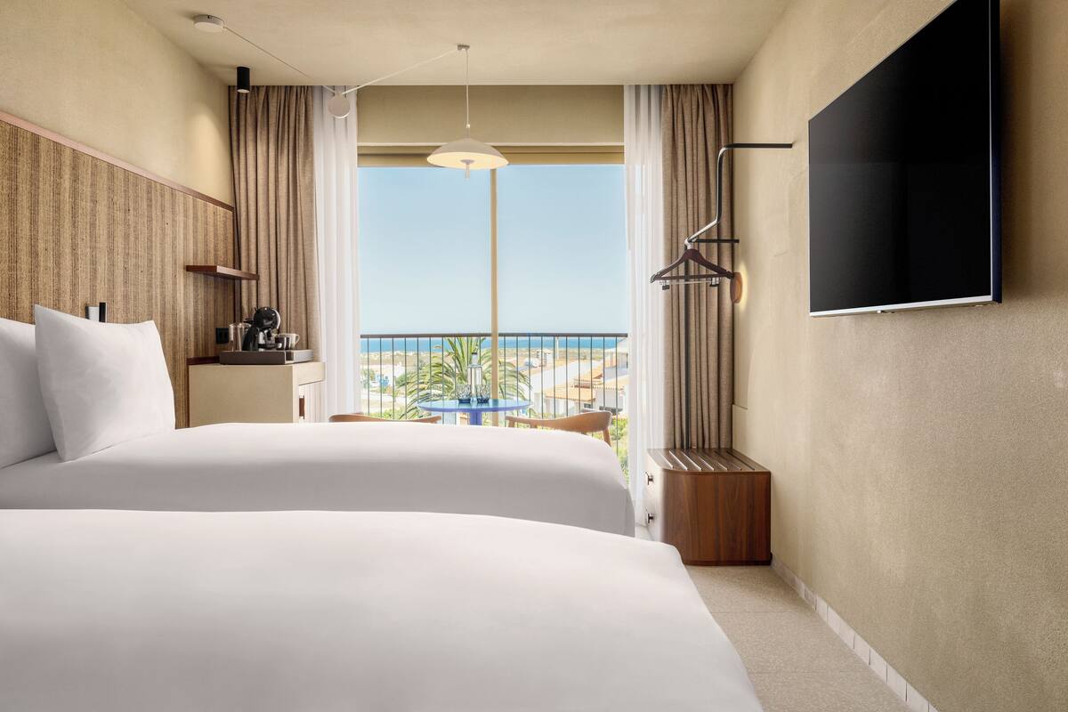 Une chambre d’hôtel avec deux lits, une télévision, une petite table avec une machine à café et vue sur la plage.