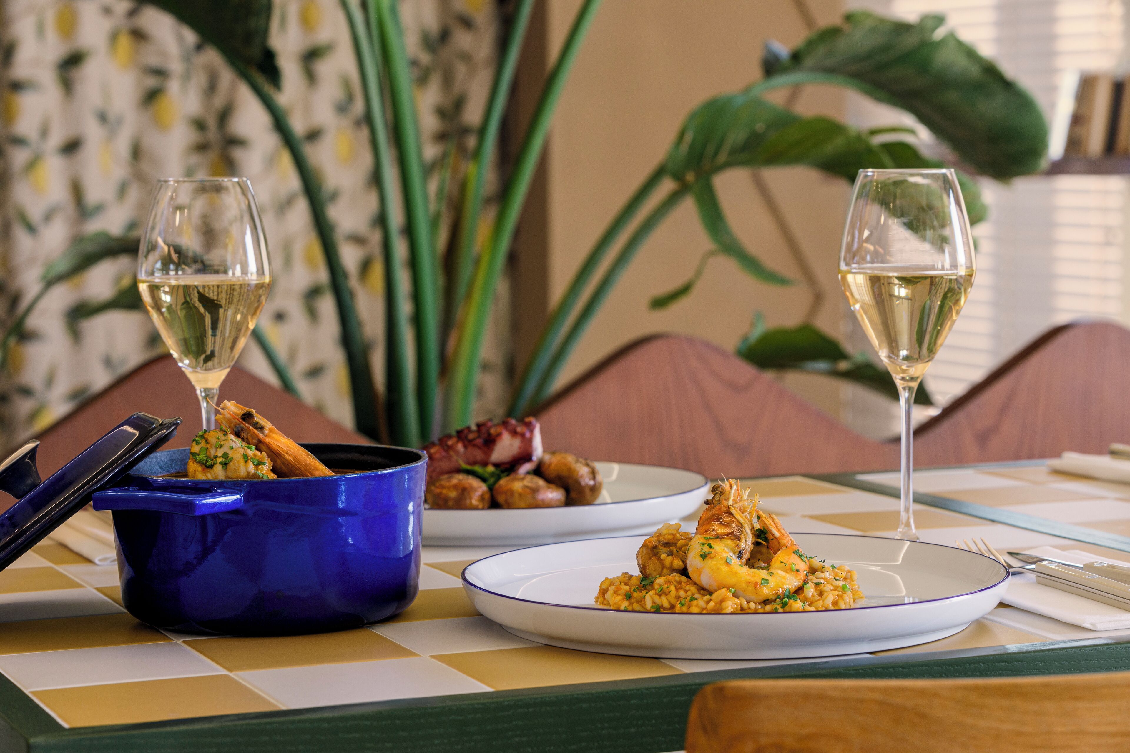 A dining table with plates of food, two glasses of white wine, and a blue bowl.