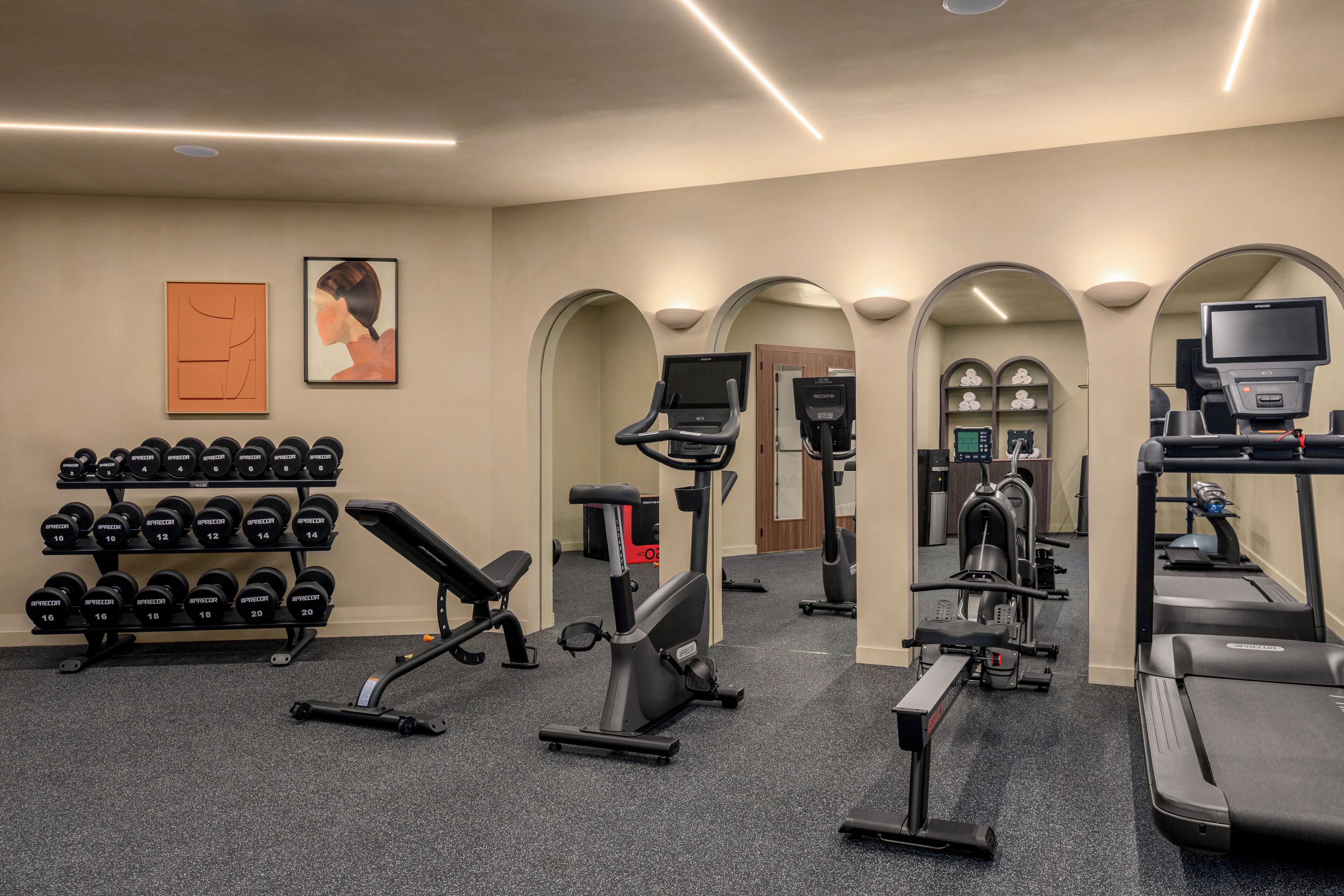 A gym with various exercise equipment, including dumbbells, an elliptical, a treadmill, and a bench.
