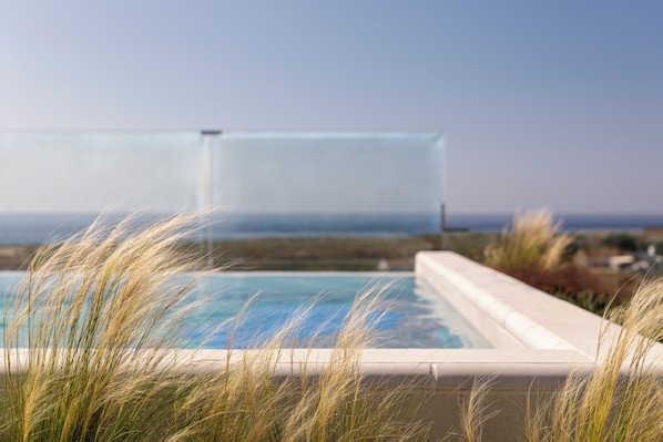 A swimming pool with a view of the ocean, surrounded by tall grass. - Amarello Hotel Praia Santo Andre, Tapestry Collection Hilton (Santiago do Cacém)