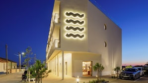 Un hotel moderno con un diseño de iluminación ondulado único en la fachada, un espacio exterior cubierto y un estacionamiento.