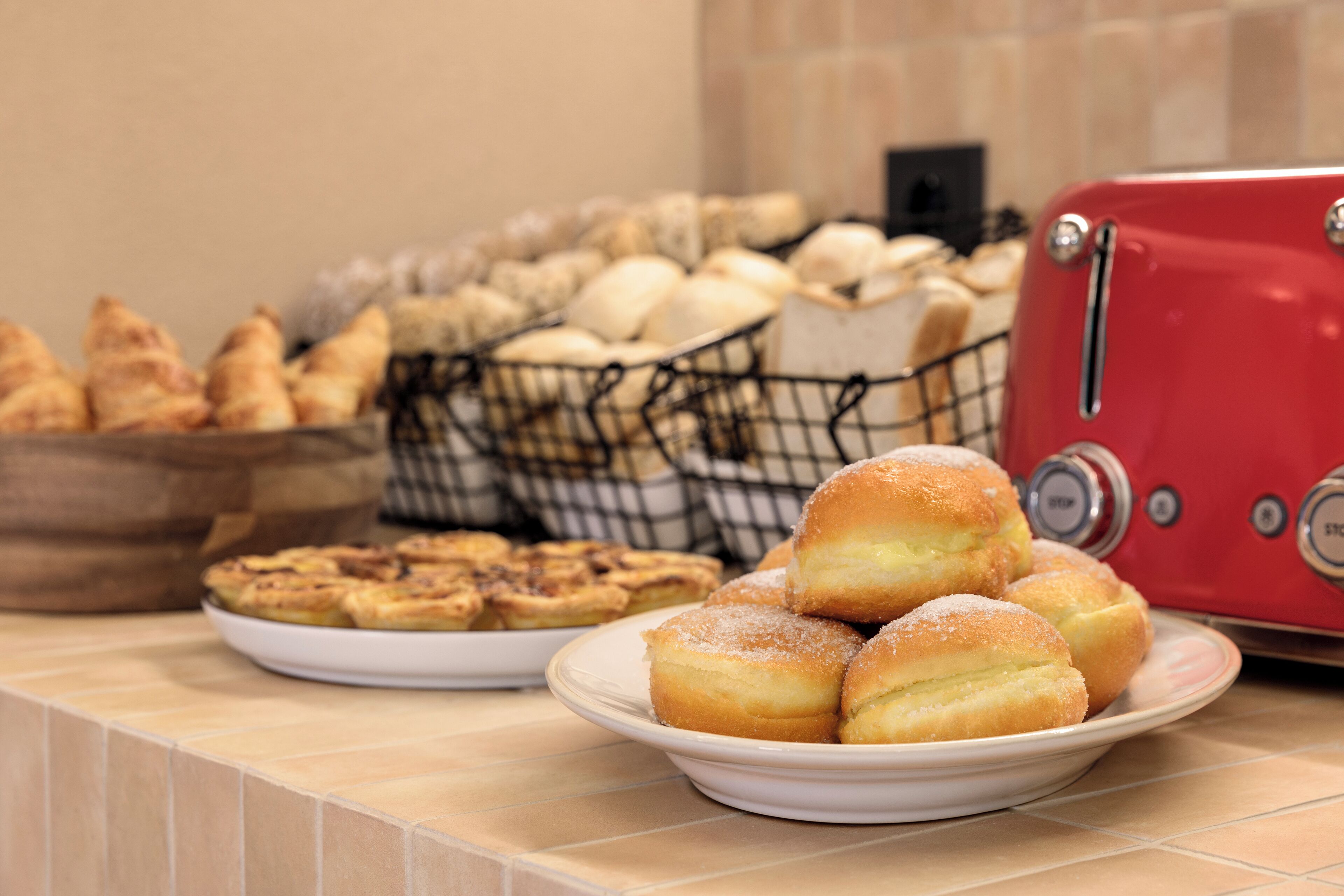 A kitchen counter with various baked goods, including pastries and bread, and a red toaster.