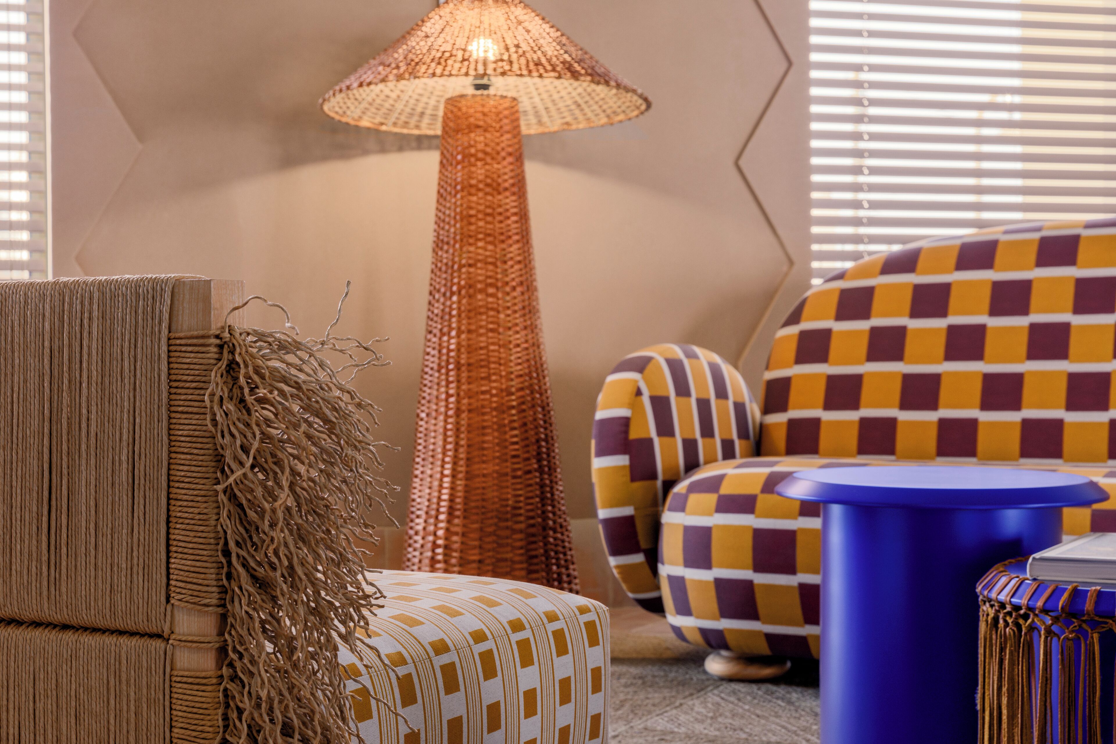 A room with a tall, woven floor lamp, a checkered sofa, and a blue side table.