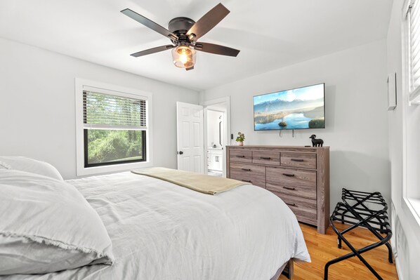 A bedroom with a bed, a ceiling fan, a dresser, a TV, and a window with blinds.