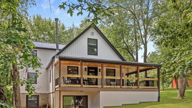 Une maison moderne à deux étages, dotée d’un grand balcon, d’un espace extérieur aménagé et couvert, et d’une pelouse bien entretenue.