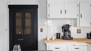 Una cucina con mobili bianchi, una porta nera con maniglie in ottone e una macchina da caffè sul piano di lavoro.