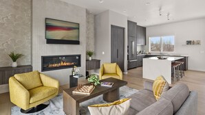 A modern living room with a fireplace, a dining area, and a kitchen with a large island. - Millpointe Main 3.0 - Luxury Meets Location: Sauna, Cold Plunge, Concerts nearby (Bend)