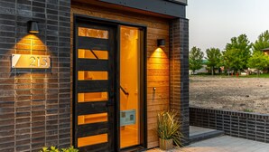 A modern building with a large glass door, a number sign '213', and two wall-mounted lights. - Millpointe Main 3.0 - Luxury Meets Location: Sauna, Cold Plunge, Concerts nearby (Bend)