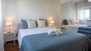 Una habitación de hotel con una cama grande, dos mesitas de noche con lámparas, un espejo y una ventana con cortinas.