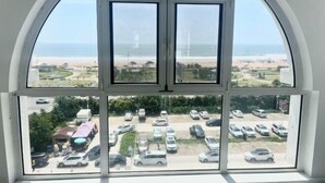 Vista a través de un amplio ventanal sobre un estacionamiento y una playa.