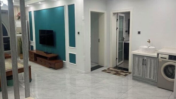 Una sala moderna con una televisión de pantalla plana, paredes de color verde azulado, un mueble de entretenimiento de madera y una lavadora.