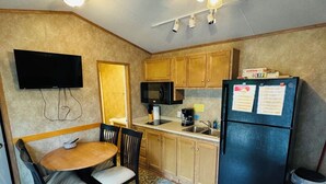 A compact kitchen with wooden cabinets, a black refrigerator, a microwave, a coffee maker, and a dining table with chairs. - Rental Cabin #403 w/ Queen bed (Wisconsin Dells)