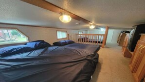 A bedroom with a bed, a window, a wooden railing, and a television.
