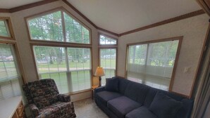 Ein Zimmer mit großem Fenster, einer Couch, einem gemusterten Sessel und einer Lampe.