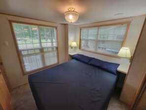 Un dormitorio con cama, dos ventanas con persianas, una lámpara de pared y un aplique de techo.