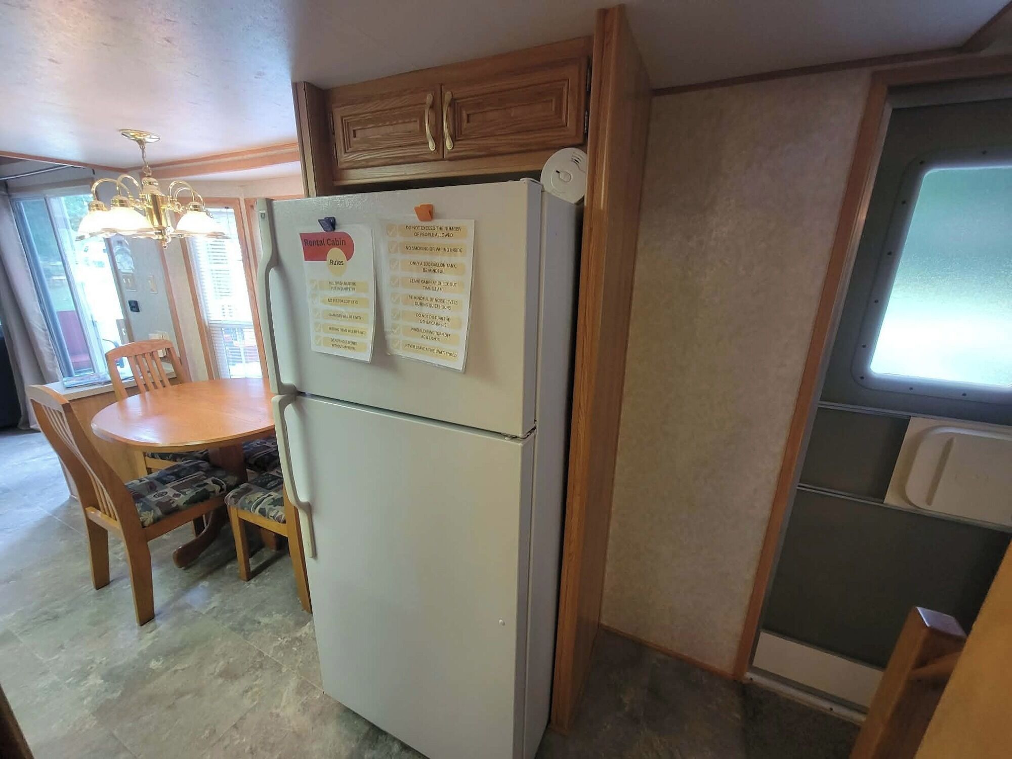 A compact kitchen with a refrigerator, wooden cabinets, a dining table with chairs, and a window.