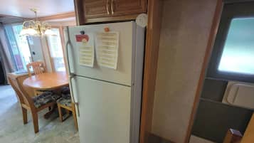 A compact kitchen with a refrigerator, wooden cabinets, a dining table with chairs, and a window.