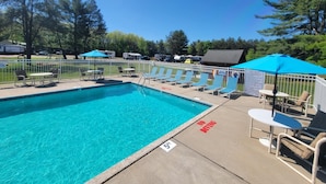 Ein Swimmingpool mit Liegestühlen und Sonnenschirmen, umgeben von einem Zaun.