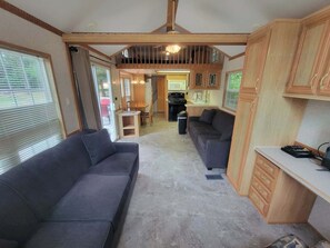 A compact RV interior with a kitchenette, a dining area, and a living space with a sofa and a desk.