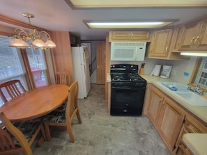 A compact kitchen with a dining table, chairs, a stove, a microwave, and wooden cabinets. - Rental Cabin #404 w/ Queen bed (Wisconsin Dells)