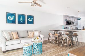 A modern living room with a white sofa, a dining table with chairs, and a kitchen area with cabinets and a microwave.