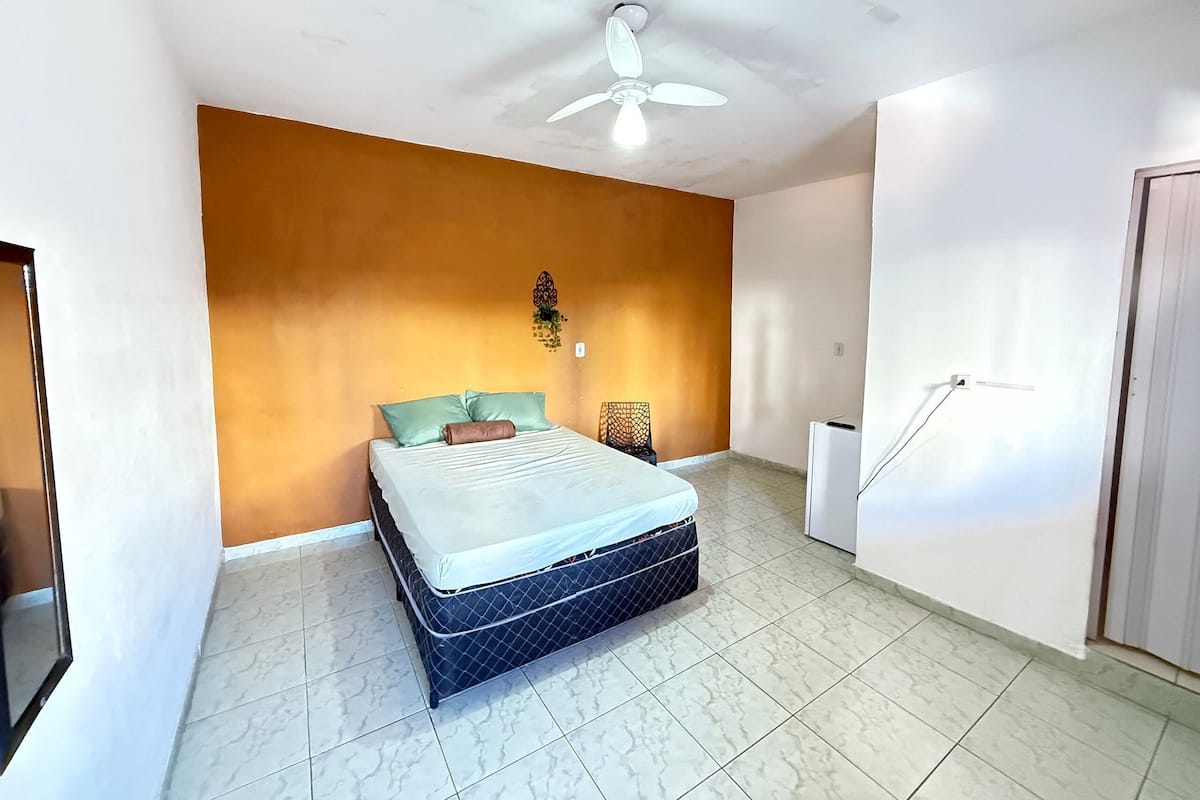 A bedroom with a bed, a ceiling fan, a wall-mounted light, and a door.