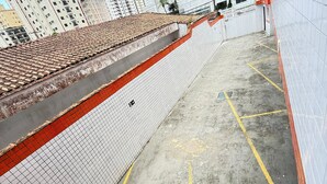 Une zone de stationnement délimitée par des lignes jaunes, un chemin piétonnier clôturé et un bâtiment doté d’un toit en tuiles.