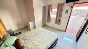 Une chambre à coucher comprenant un lit, une chaise, un téléviseur, une fenêtre avec des rideaux et une porte donnant sur l’extérieur.