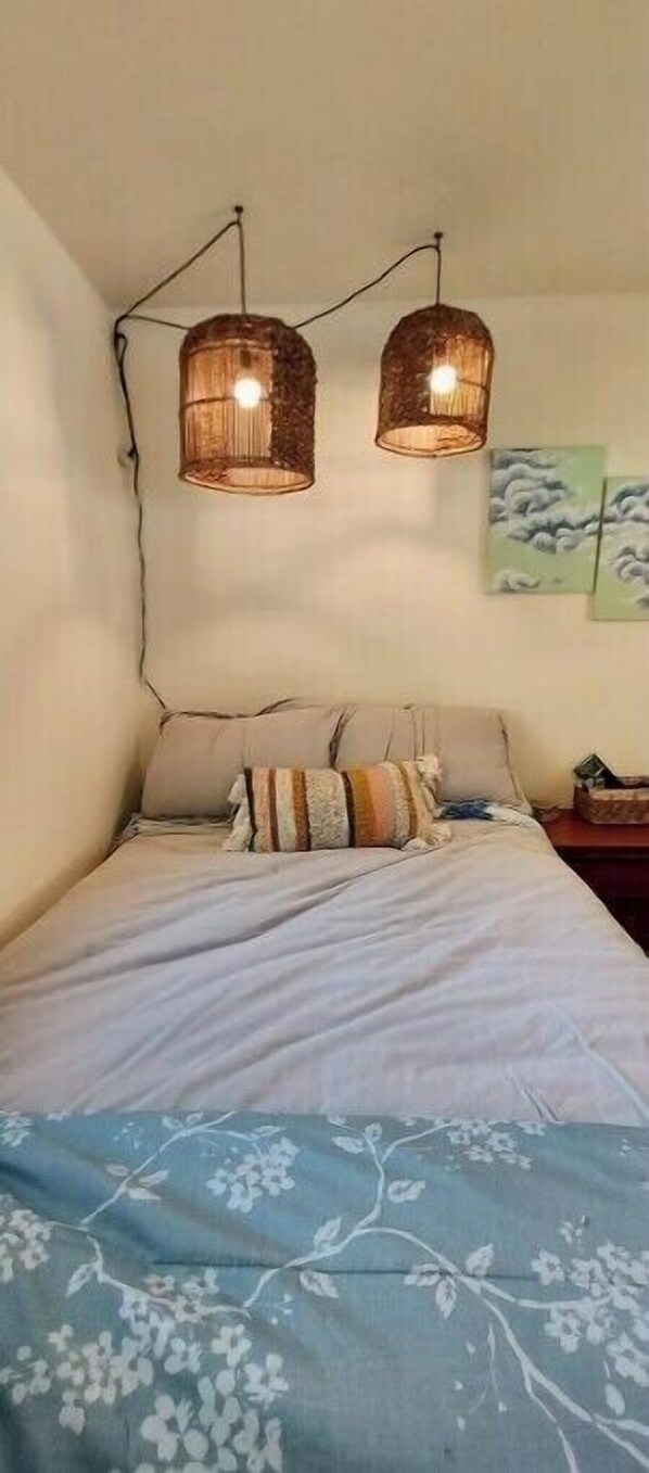 A bedroom with a bed, two hanging lamps, and a painting on the wall.