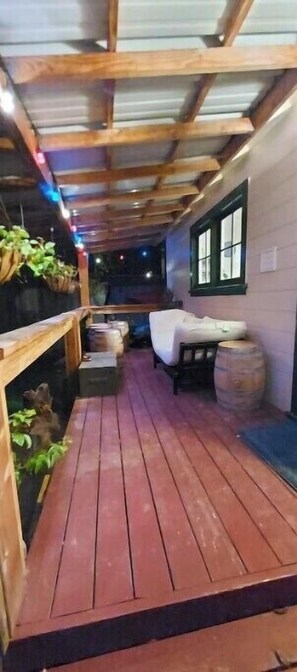 A wooden deck with a sofa and a barrel, surrounded by walls and a window.