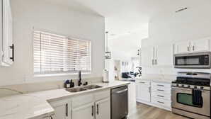 A modern kitchen with white cabinets, stainless steel appliances, and a wooden floor.