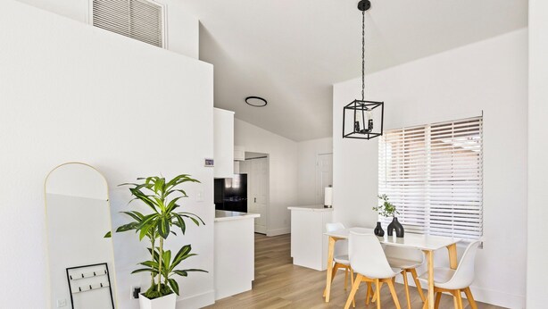 A modern, white interior with a dining area, a potted plant, and a kitchen in the background.