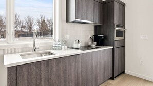A modern kitchen with dark wood cabinets, a stainless steel range hood, and a built-in oven. - Millpointe Studio 1.0 - Where Luxury Meets Location -Steps to Concerts, Old Mill (Bend)