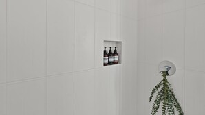 A bathroom with white tiles, a showerhead, and three bottles of shampoo in a recessed shelf. - Millpointe Studio 1.0 - Where Luxury Meets Location -Steps to Concerts, Old Mill (Bend)