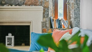 A cozy living room with a fireplace, a bookshelf, and a window with books on the sill.