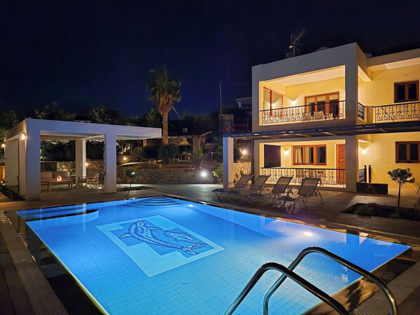 A modern two-story house with a swimming pool, outdoor seating, and a well-lit balcony.