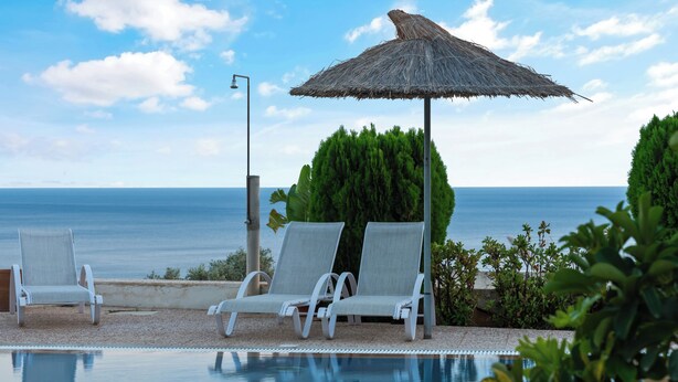 A poolside area with lounge chairs and a thatched umbrella, overlooking the sea.