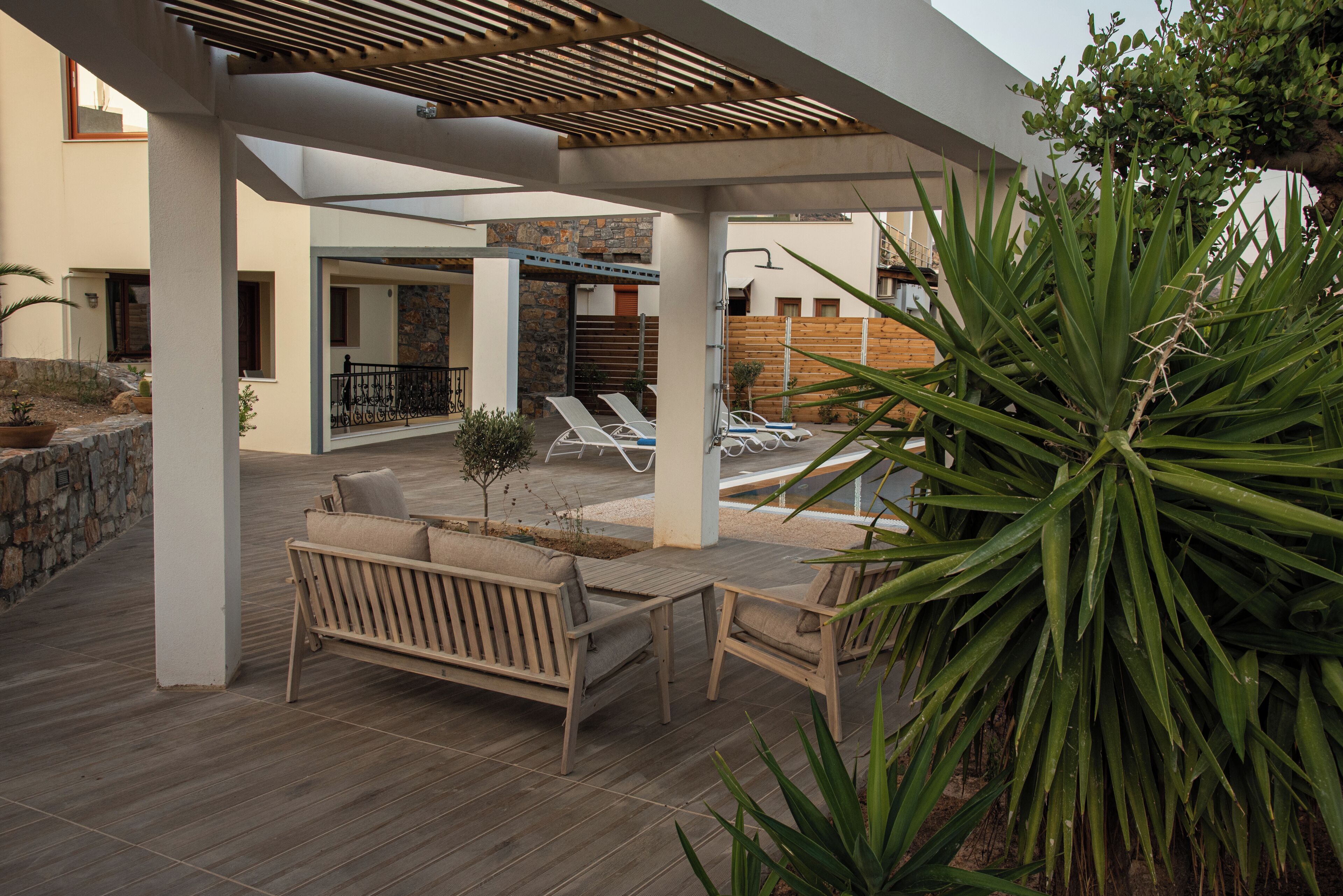 An outdoor patio area with wooden flooring, a wooden bench, a table, and a potted plant.